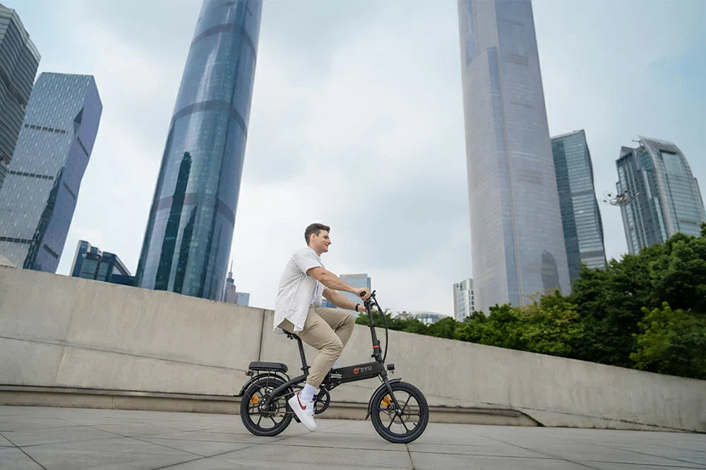 Modern city lifestyle shot of a man riding matte black DYU AF PRO compact foldable e-bike on concrete plaza surrounded by glass skyscrapers.