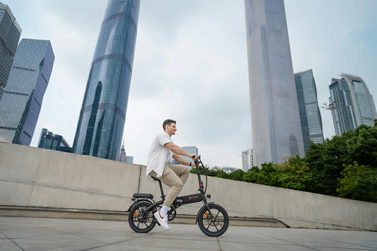 Modern city lifestyle shot of a man riding matte black DYU AF PRO compact foldable e-bike on concrete plaza surrounded by glass skyscrapers.