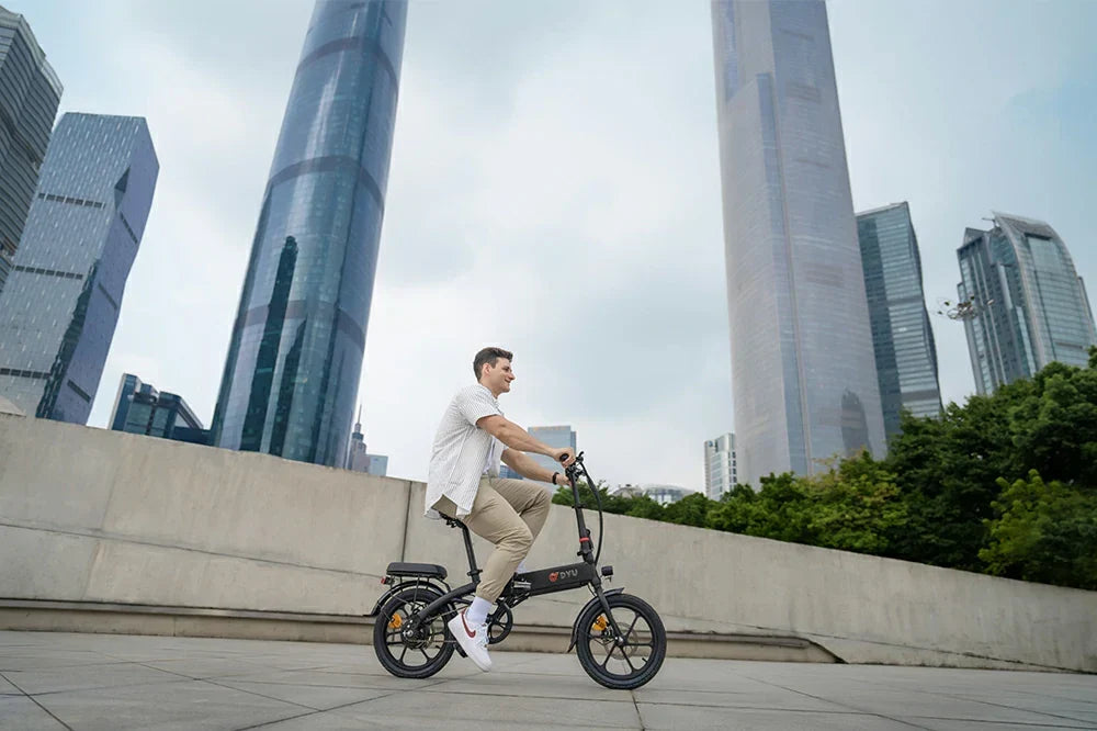 Modern city lifestyle shot of a man riding matte black DYU AF PRO compact foldable e-bike on concrete plaza surrounded by glass skyscrapers.